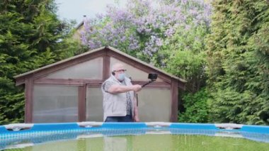 Ciddi yaşlı bir adam siyah tripodu tutuyor ve video çekiyor.