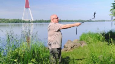 Yaşlı adam modern selfie çubuğu tutuyor ve video çekiyor.