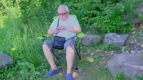 Pensionné assis dans le fauteuil et nettoie la lentille photo avec lingette — Video