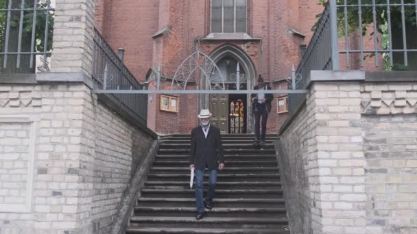 Senior geht in der Nähe der Kirche Treppe hinunter, während Mann Video dreht — Stockvideo