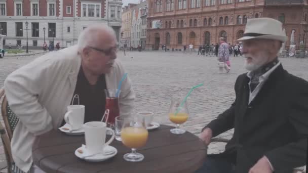 Senior mænd sætter sig ned på stole ved lille bord med drikkevarer – Stock-video