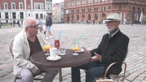 Pensionärer kommunicerar sittande vid bordet i mysiga street cafe — Stockvideo