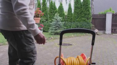 Olgun adam hortumu makaranın üzerine açar bahçedeki çimleri sular.