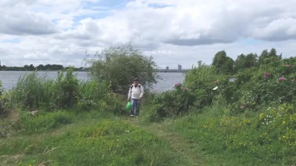 Homem maduro com mochila caminha ao longo do caminho rural na margem do rio — Vídeo de Stock