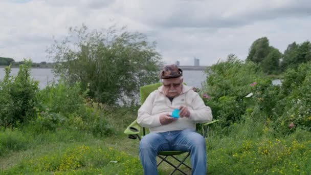 Pensionista despega y limpia lupa en la orilla del río — Vídeos de Stock