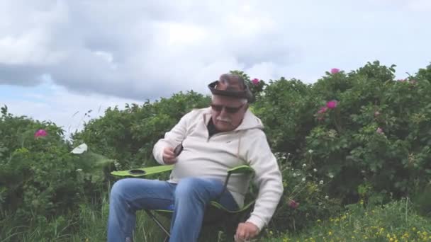 Пенсионер чистит увеличительное стекло возле цветущих кустов — стоковое видео