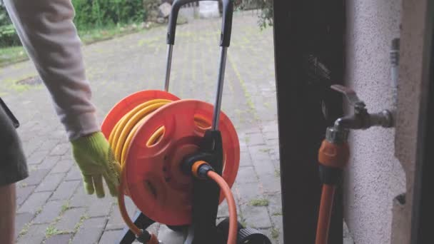 Mann zieht Sprinkler aus Schlauch auf Rollwagen im Hof — Stockvideo