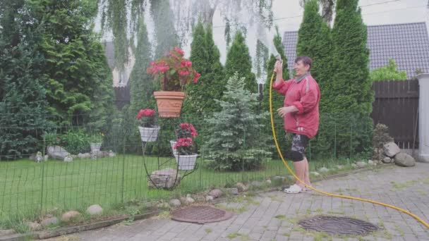 Glückliche Rentnerin bewässert saftigen Rasen im Hausgarten mit Schlauch — Stockvideo