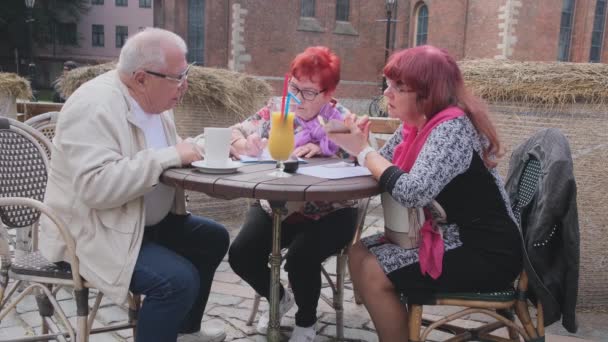 Старший чоловік розмовляє з жінками з яскравим волоссям, сидячи в кафе — стокове відео