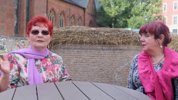 Las mujeres mayores con bufandas brillantes hablan en la mesa en la cafetería — Vídeos de Stock