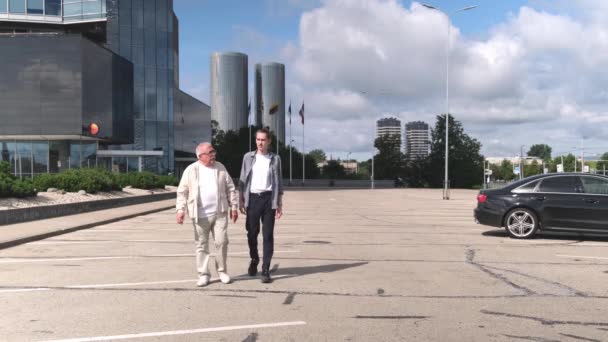 Ceketli yaşlı bir adam ve şehirde otoparkta yürüyen bir adam. — Stok video