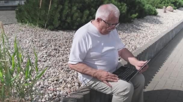 Hombre mayor con tipos de gafas en el ordenador portátil sentado en parapeto — Vídeos de Stock