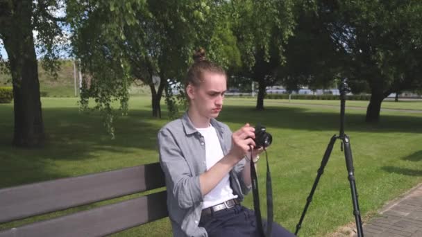 Mladý muž ladí fotoaparát a fotí sezení v zahradě — Stock video