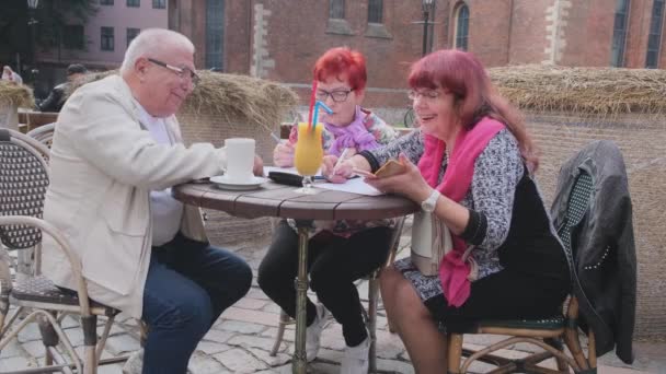 Hombre y mujeres mayores trabajan con papeles en restaurante callejero — Vídeos de Stock