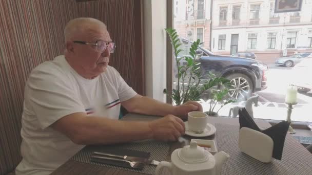 Hombre mayor bebe té esperando la cena en la mesa en la cafetería — Vídeo de stock