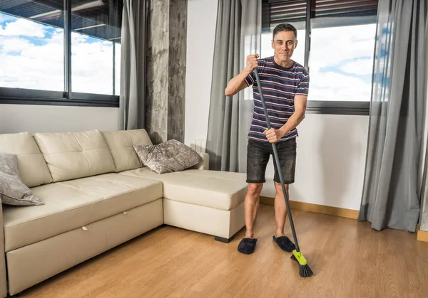Smiling man in casual clothes and slippers sweeping his living room. Full body.