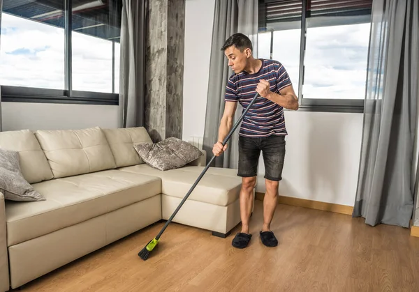 Man in casual clothes and slippers sweeping his living room. Full body.