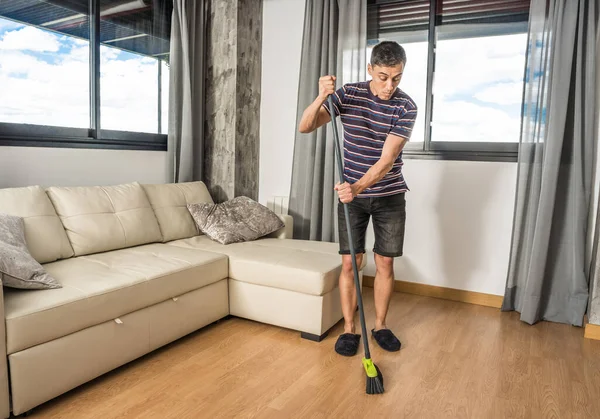 Man in casual clothes and slippers sweeping his living room. Full body.