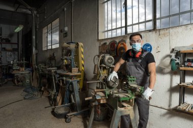 Fabrikada maske ve koruyucu ekipmanla duran bir işçi. Orta çekim.