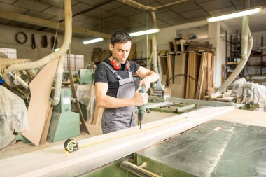 Fabrikada matkapla çalışan koruyucu ekipmanlarla çalışan bir işçi. Orta çekim.