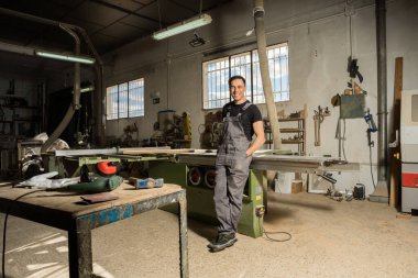 İşçi fabrikada kameraya bakıp gülümsüyor. Uzun atış, tüm vücut..