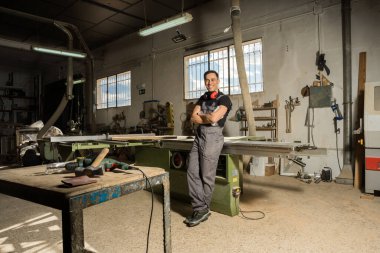 İşçi koruyucu aletlerle dikilip bir fabrikada gülümseyen kameraya bakıyor. Uzun atış, tüm vücut..