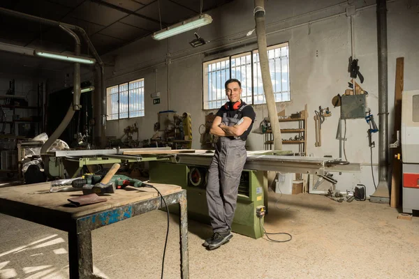 İşçi koruyucu aletlerle dikilip bir fabrikada gülümseyen kameraya bakıyor. Uzun atış, tüm vücut..