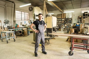 İşçi bir fabrikada kameraya bakıyor. Tam vücut, uzun atış..