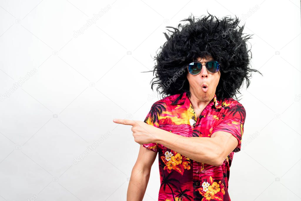 Man in afro wig, sunglasses and hawaiian shirt, pointing aside very surprised. Mid shot. White background.