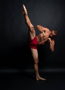 İç çamaşırlı atletik bir adam tekme atıyor. Tam vücut. Siyah arkaplan.