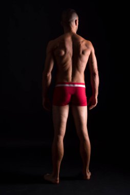 İç çamaşırlı atletik bir adam. Tüm vücut, geriye. Siyah arkaplan.