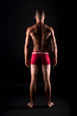 İç çamaşırlı atletik bir adam. Tüm vücut, geriye. Siyah arkaplan.