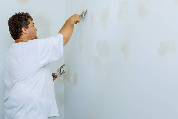 Male builder repairs wall with a spatula plaster on a wall