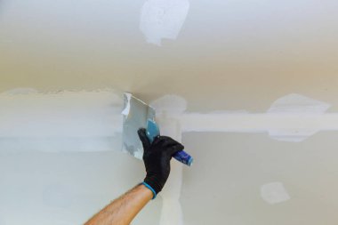 Boya spatulası kullanan işçiler alçıtaşı sıva tamiri yapıyor.