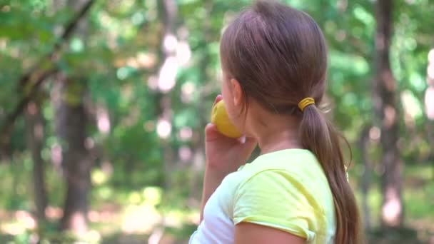 Barn flicka äter ett rött äpple i en park i naturen. — Stockvideo