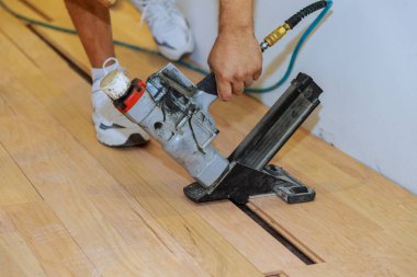 Skilled worker during the installation of pre-finished interlocking parquet. Installation of oak use pneumatic hammer parquet on an existing floor. clipart
