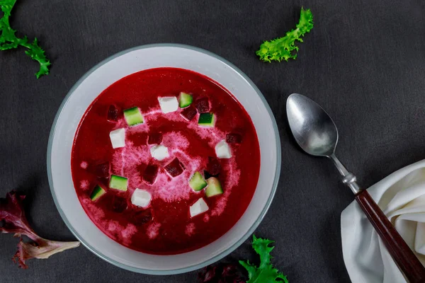 Bowl of cream soup of red beets with a fresh beet root and leaves on rustic table