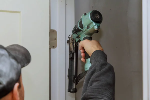 Montaż drzwi pokoju w domu pracownik drewna za pomocą pistoletu do paznokci — Zdjęcie stockowe