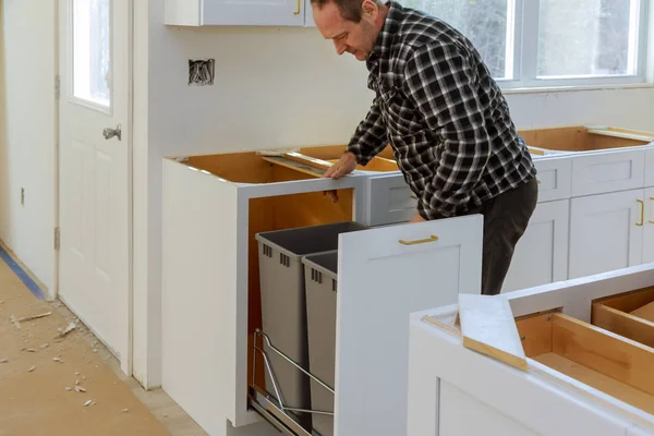 Handyman in installed drawers garbage bin in the kitchen