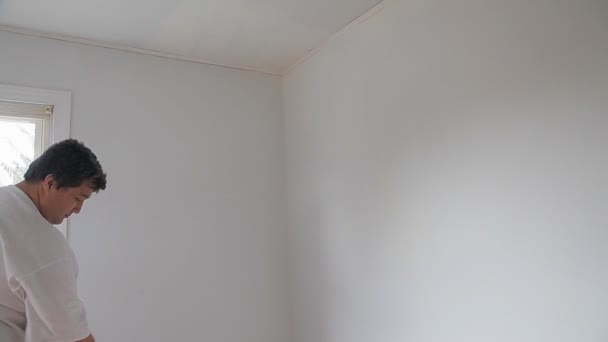 El hombre está pintando un hace reparaciones en el apartamento con un rodillo de pintura haciendo pintura de pared — Vídeos de Stock