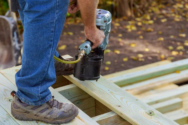 Handyman verandada ahşap döşeme yükleme, çivi tabancası kullanarak çalışıyor çivi