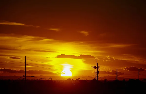 Um belo pôr do sol com cores laranja e amarela no céu as montanhas e palmeiras em silhueta na distância Arizona . — Fotografia de Stock