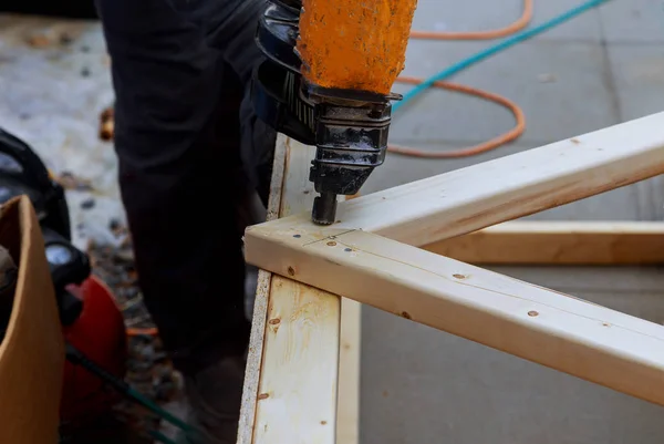 Man building a wooden patio with hammering screwing together beams