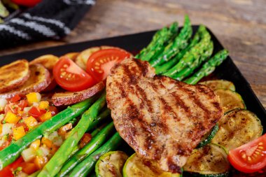 Izgara biftek, patates ve kuşkonmaz siyah tabakta