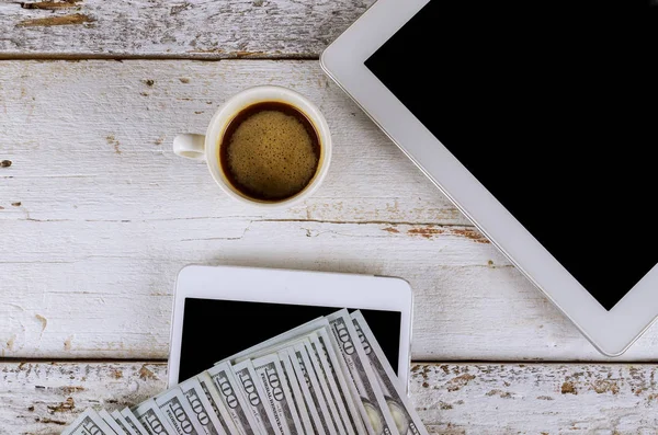 Tablet mockup on work desk with cup of coffee and US dollar banknote space beside for text. Flat lay composition.