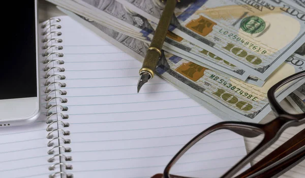 As notas de dólar, close-up estão em uma folha de papel branca ao lado de uma caneta e óculos em uma moldura de plástico — Fotografia de Stock