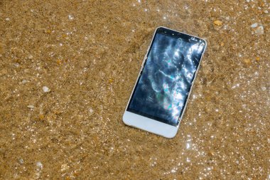 Kırık çöktü akıllı telefon suda yatıyor. Kumlu plajda telefon