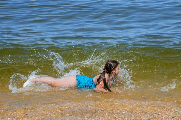 Усміхнена маленька дівчинка лежить у воді на узбережжі пляжу це океан . — стокове фото