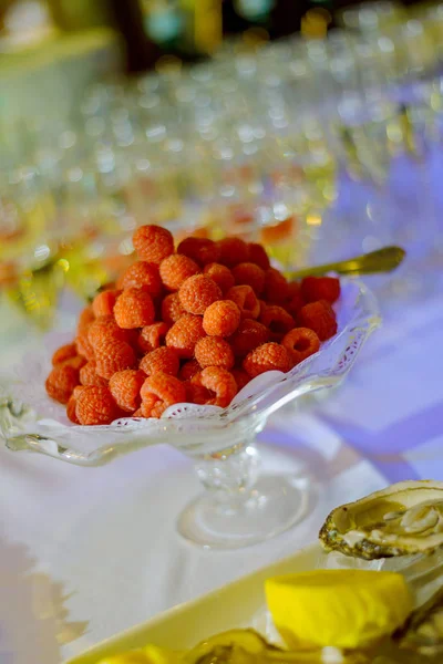 Cuenco de cristal de frambuesas en la mesa blanca y muchos vasos de vino de fondo —  Fotos de Stock