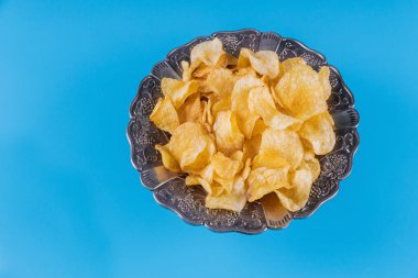 Mavi arka plan üzerinde gümüş bir kapta gevrek patates cipsi.